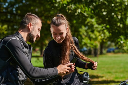 A sweet couple, equipped with bicycles and engrossed in coordinating their journey, checks their GPS mobile and watches while planning scenic routes in the park, seamlessly blending technology and outdoor adventure for a delightful cycling experience.