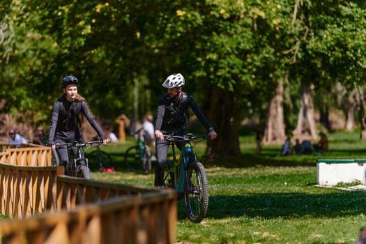 A blissful couple, adorned in professional cycling gear, enjoys a romantic bicycle ride through a park, surrounded by modern natural attractions, radiating love and happiness.