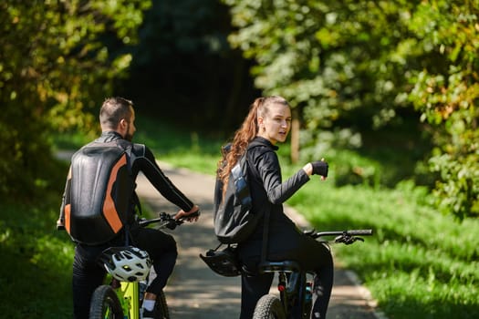 A blissful couple, adorned in professional cycling gear, enjoys a romantic bicycle ride through a park, surrounded by modern natural attractions, radiating love and happiness.