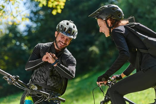 A sweet couple, equipped with bicycles and engrossed in coordinating their journey, checks their GPS mobile and watches while planning scenic routes in the park, seamlessly blending technology and outdoor adventure for a delightful cycling experience.