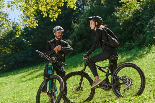 A sweet couple, equipped with bicycles and engrossed in coordinating their journey, checks their GPS mobile and watches while planning scenic routes in the park, seamlessly blending technology and outdoor adventure for a delightful cycling experience.