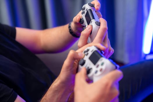 Close up of photo in holding joystick, playing video game or online streamer with friends in neon blue light curtain background. Concept of sitting couch lifestyles gamer in living room. Sellable.