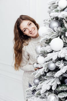 woman decorates white Christmas tree with new year gifts