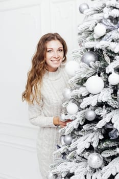 woman decorates white Christmas tree with new year gifts