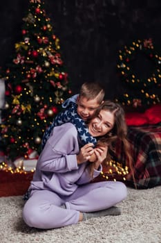 woman with son decorates white Christmas tree with new year gifts