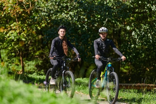 A blissful couple, adorned in professional cycling gear, enjoys a romantic bicycle ride through a park, surrounded by modern natural attractions, radiating love and happiness.