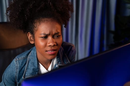 Young African American creator woman with serious face, thinking carefully and looking at final project document on laptop for planing next sequence. Concept of work at neat home place. Tastemaker.