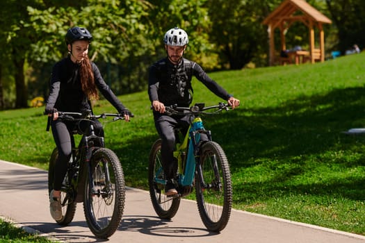 A blissful couple, adorned in professional cycling gear, enjoys a romantic bicycle ride through a park, surrounded by modern natural attractions, radiating love and happiness.