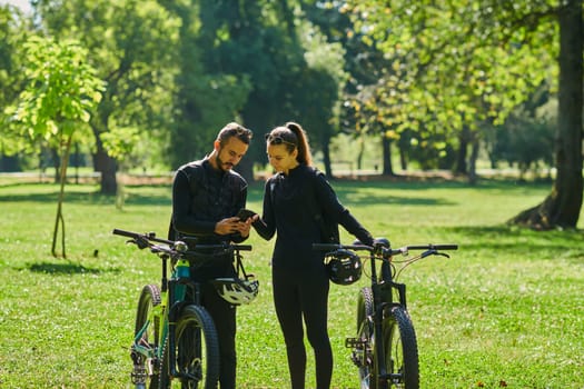 A sweet couple, equipped with bicycles and engrossed in coordinating their journey, checks their GPS mobile and watches while planning scenic routes in the park, seamlessly blending technology and outdoor adventure for a delightful cycling experience.