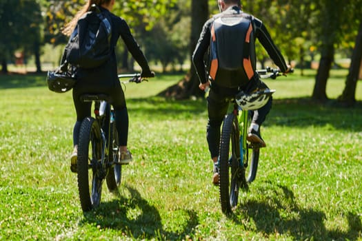 A blissful couple, adorned in professional cycling gear, enjoys a romantic bicycle ride through a park, surrounded by modern natural attractions, radiating love and happiness.