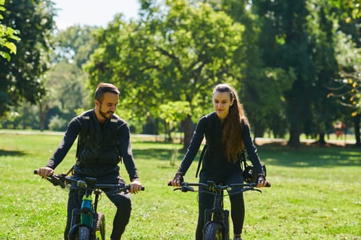 A blissful couple, adorned in professional cycling gear, enjoys a romantic bicycle ride through a park, surrounded by modern natural attractions, radiating love and happiness.