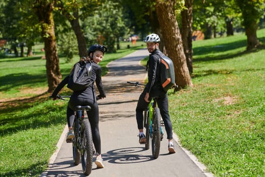 A blissful couple, adorned in professional cycling gear, enjoys a romantic bicycle ride through a park, surrounded by modern natural attractions, radiating love and happiness.