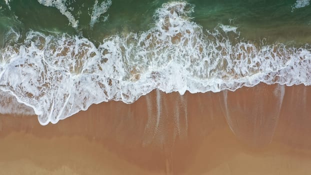Sea wave on beach aerial view. Coast with waves as background from top view. Wave with sea foam background from drone. Aerial view of beach with waves of sea water