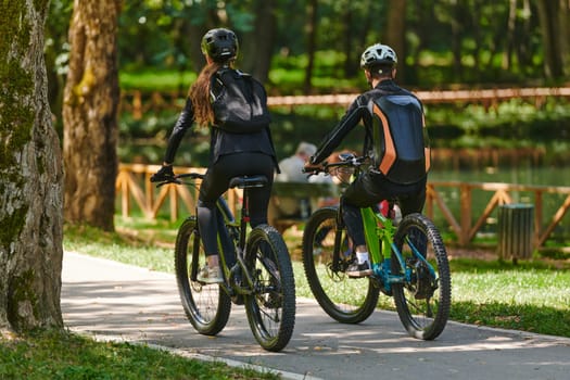 A blissful couple, adorned in professional cycling gear, enjoys a romantic bicycle ride through a park, surrounded by modern natural attractions, radiating love and happiness.