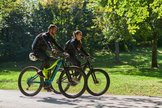 A blissful couple, adorned in professional cycling gear, enjoys a romantic bicycle ride through a park, surrounded by modern natural attractions, radiating love and happiness.