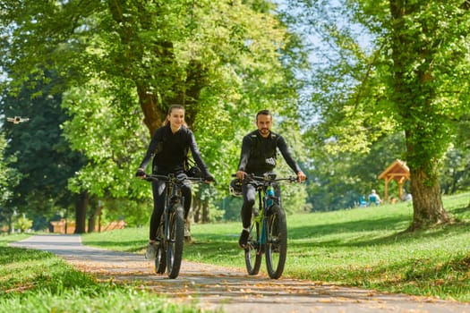 A blissful couple, adorned in professional cycling gear, enjoys a romantic bicycle ride through a park, surrounded by modern natural attractions, radiating love and happiness.