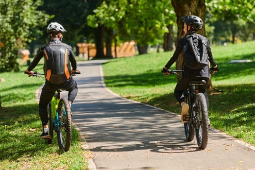 A blissful couple, adorned in professional cycling gear, enjoys a romantic bicycle ride through a park, surrounded by modern natural attractions, radiating love and happiness.