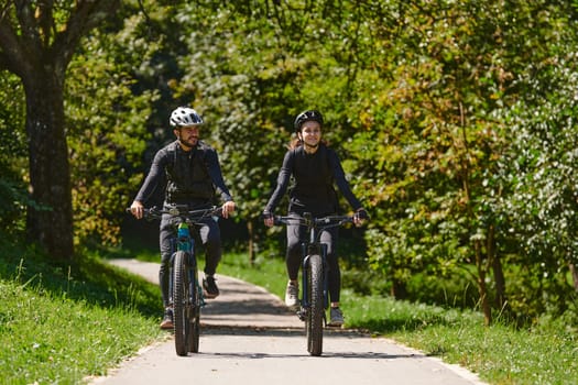 A blissful couple, adorned in professional cycling gear, enjoys a romantic bicycle ride through a park, surrounded by modern natural attractions, radiating love and happiness.