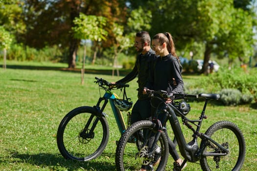 A blissful couple, adorned in professional cycling gear, enjoys a romantic bicycle ride through a park, surrounded by modern natural attractions, radiating love and happiness.