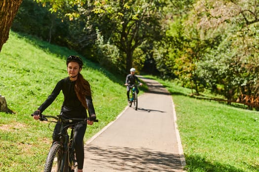 A blissful couple, adorned in professional cycling gear, enjoys a romantic bicycle ride through a park, surrounded by modern natural attractions, radiating love and happiness.