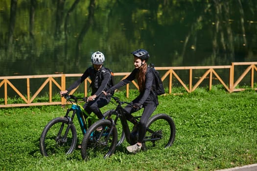 A blissful couple, adorned in professional cycling gear, enjoys a romantic bicycle ride through a park, surrounded by modern natural attractions, radiating love and happiness.