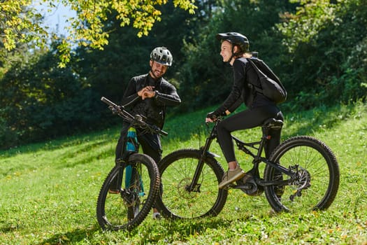 A sweet couple, equipped with bicycles and engrossed in coordinating their journey, checks their GPS mobile and watches while planning scenic routes in the park, seamlessly blending technology and outdoor adventure for a delightful cycling experience.