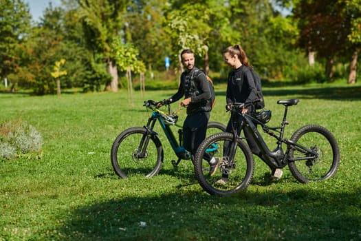 A blissful couple, adorned in professional cycling gear, enjoys a romantic bicycle ride through a park, surrounded by modern natural attractions, radiating love and happiness.