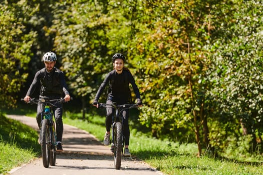 A blissful couple, adorned in professional cycling gear, enjoys a romantic bicycle ride through a park, surrounded by modern natural attractions, radiating love and happiness.