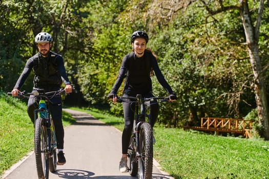 A blissful couple, adorned in professional cycling gear, enjoys a romantic bicycle ride through a park, surrounded by modern natural attractions, radiating love and happiness.