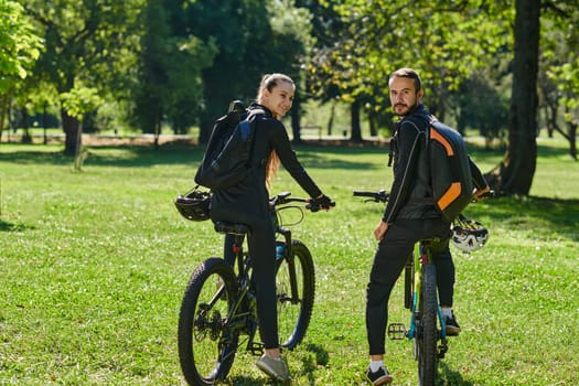 A blissful couple, adorned in professional cycling gear, enjoys a romantic bicycle ride through a park, surrounded by modern natural attractions, radiating love and happiness.