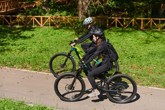 A blissful couple, adorned in professional cycling gear, enjoys a romantic bicycle ride through a park, surrounded by modern natural attractions, radiating love and happiness.