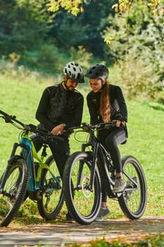 A sweet couple, equipped with bicycles and engrossed in coordinating their journey, checks their GPS mobile and watches while planning scenic routes in the park, seamlessly blending technology and outdoor adventure for a delightful cycling experience.