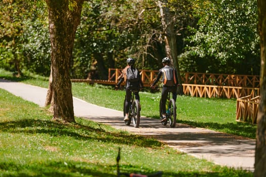 A blissful couple, adorned in professional cycling gear, enjoys a romantic bicycle ride through a park, surrounded by modern natural attractions, radiating love and happiness.