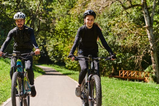 A blissful couple, adorned in professional cycling gear, enjoys a romantic bicycle ride through a park, surrounded by modern natural attractions, radiating love and happiness.