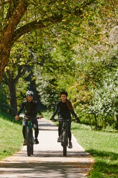 A blissful couple, adorned in professional cycling gear, enjoys a romantic bicycle ride through a park, surrounded by modern natural attractions, radiating love and happiness.