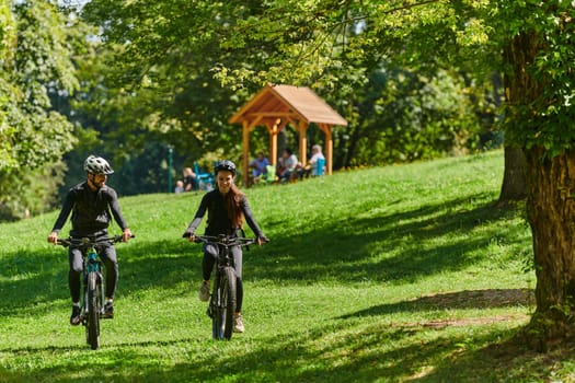 A blissful couple, adorned in professional cycling gear, enjoys a romantic bicycle ride through a park, surrounded by modern natural attractions, radiating love and happiness.