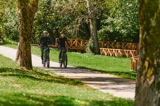 A blissful couple, adorned in professional cycling gear, enjoys a romantic bicycle ride through a park, surrounded by modern natural attractions, radiating love and happiness.