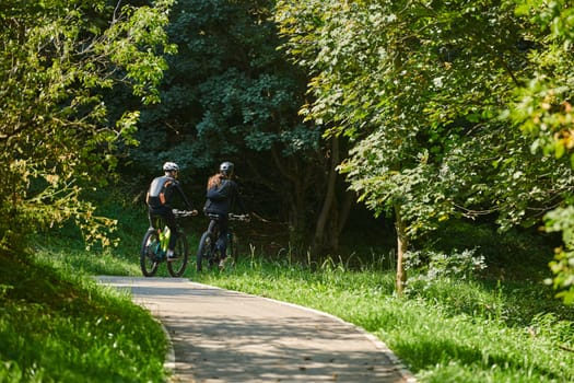 A blissful couple, adorned in professional cycling gear, enjoys a romantic bicycle ride through a park, surrounded by modern natural attractions, radiating love and happiness.