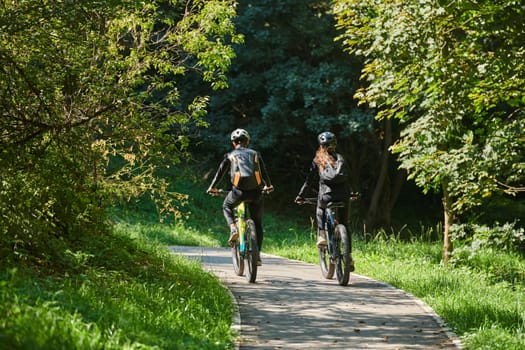 A blissful couple, adorned in professional cycling gear, enjoys a romantic bicycle ride through a park, surrounded by modern natural attractions, radiating love and happiness.