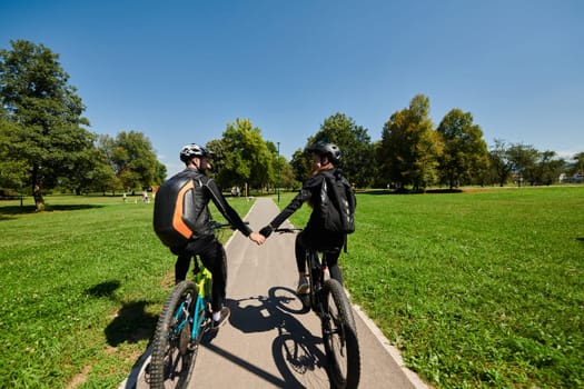 A sweet couple, adorned in cycling gear, rides their bicycles, their hands interlocked in a romantic embrace, capturing the essence of love, adventure, and joy on a sunlit path.