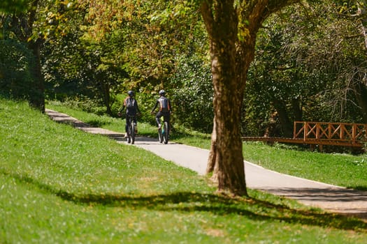 A blissful couple, adorned in professional cycling gear, enjoys a romantic bicycle ride through a park, surrounded by modern natural attractions, radiating love and happiness.