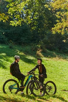 A sweet couple, equipped with bicycles and engrossed in coordinating their journey, checks their GPS mobile and watches while planning scenic routes in the park, seamlessly blending technology and outdoor adventure for a delightful cycling experience.