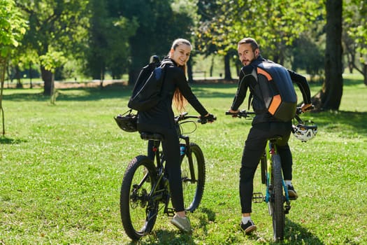 A blissful couple, adorned in professional cycling gear, enjoys a romantic bicycle ride through a park, surrounded by modern natural attractions, radiating love and happiness.