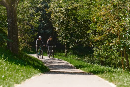 A blissful couple, adorned in professional cycling gear, enjoys a romantic bicycle ride through a park, surrounded by modern natural attractions, radiating love and happiness.