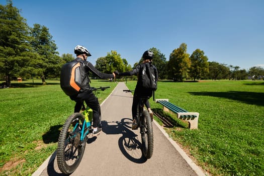 A sweet couple, adorned in cycling gear, rides their bicycles, their hands interlocked in a romantic embrace, capturing the essence of love, adventure, and joy on a sunlit path.