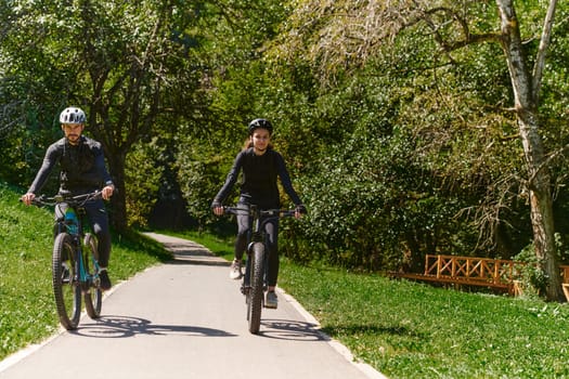 A blissful couple, adorned in professional cycling gear, enjoys a romantic bicycle ride through a park, surrounded by modern natural attractions, radiating love and happiness.