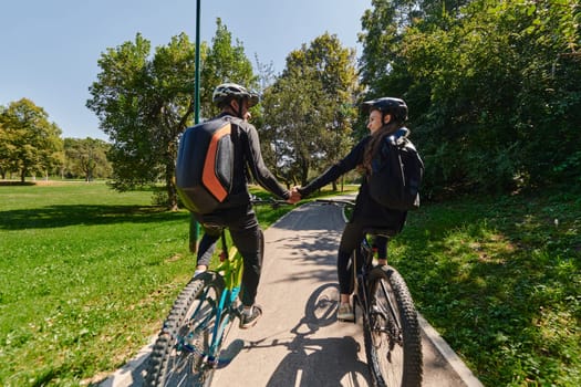 A sweet couple, adorned in cycling gear, rides their bicycles, their hands interlocked in a romantic embrace, capturing the essence of love, adventure, and joy on a sunlit path.