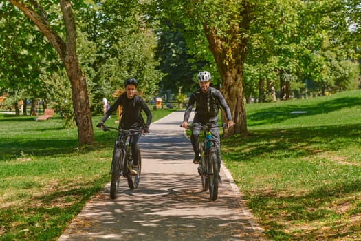 A blissful couple, adorned in professional cycling gear, enjoys a romantic bicycle ride through a park, surrounded by modern natural attractions, radiating love and happiness.