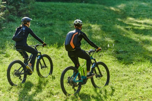 A blissful couple, adorned in professional cycling gear, enjoys a romantic bicycle ride through a park, surrounded by modern natural attractions, radiating love and happiness.