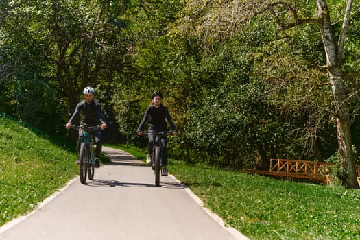 A blissful couple, adorned in professional cycling gear, enjoys a romantic bicycle ride through a park, surrounded by modern natural attractions, radiating love and happiness.